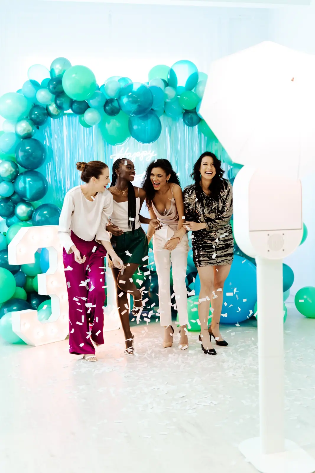 Friends celebrating with confetti at a colorful event backdrop